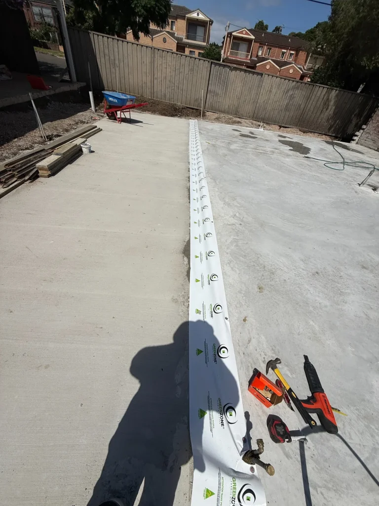A prepared treatment line along a concrete perimeter during barrier installation work.