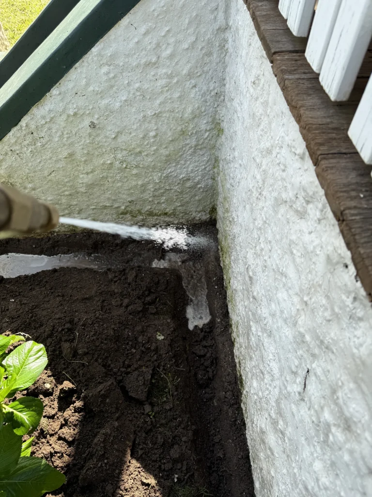 A trench being treated alongside an external foundation wall as part of termite-management work.