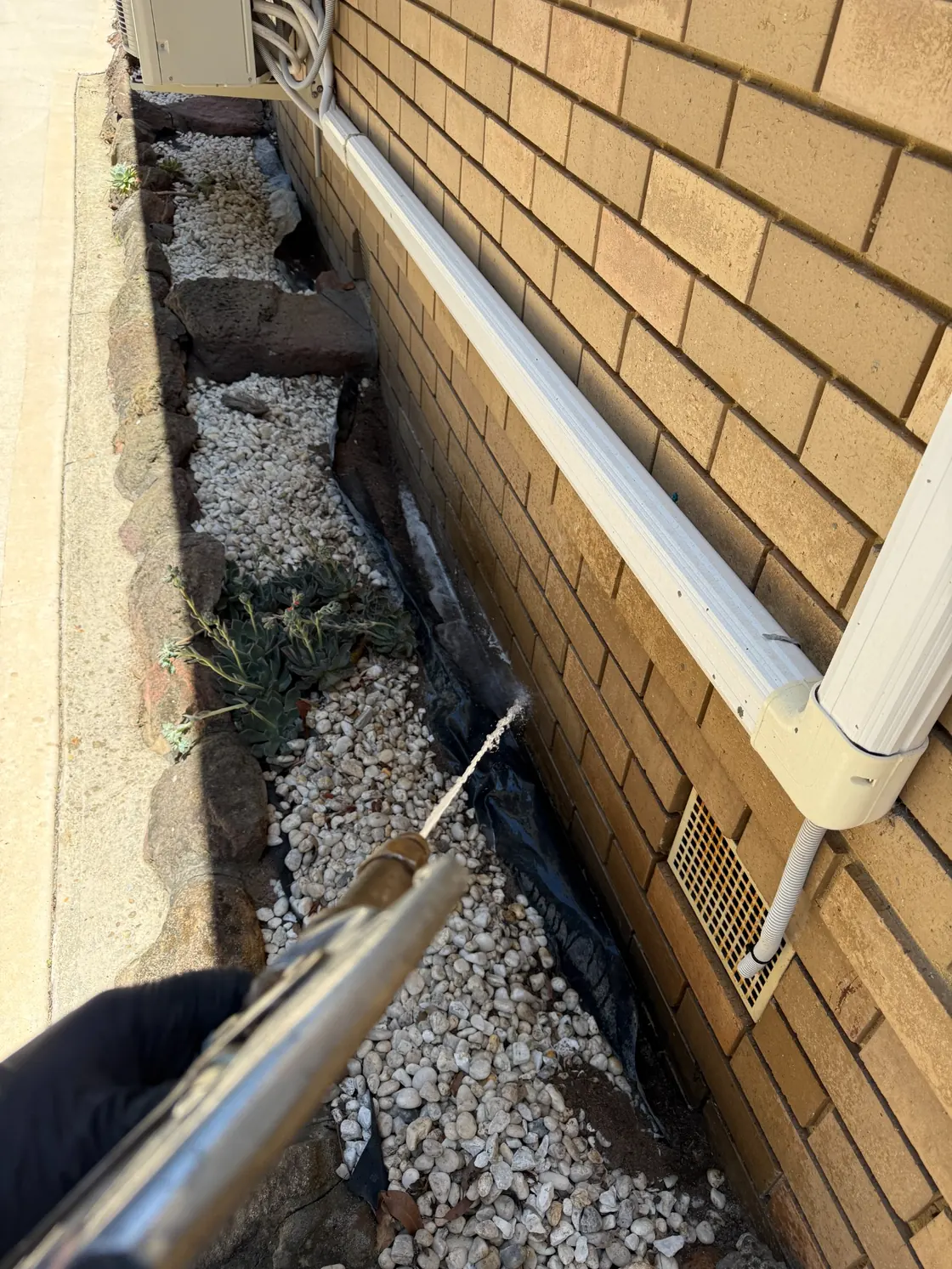 Termidor HE soil treatment within external gravel garden bed beside brick wall in Epping