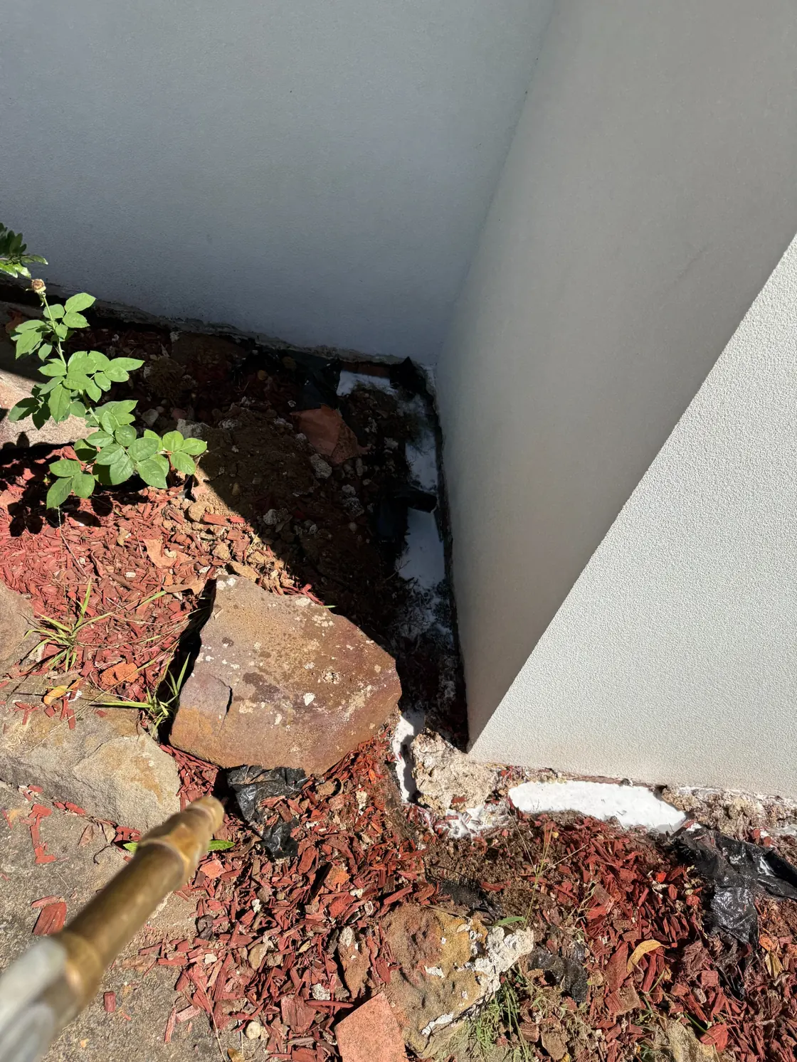 Termite prevention soil treatment at exterior wall corner with gravel and landscaping in Epping